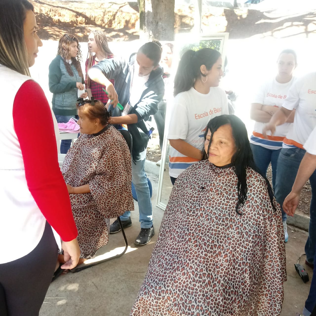 Duas mulheres com a toalha de proteção, arrumam o cabelo, atendidas por cabeleireiras voluntárias do Bairro da Gente